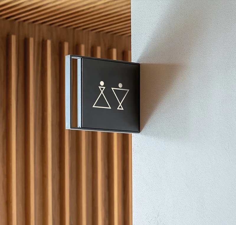 Modern hotel toilet sign with Khai Hotel brand identity icons on a concrete wall