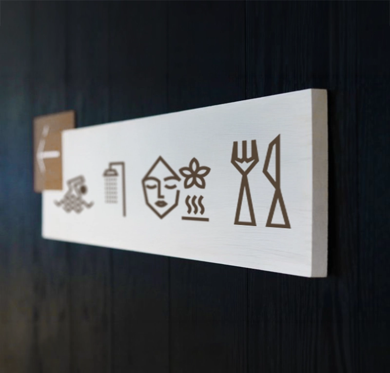 Khai Hotel indoor wayfinding sign featuring custom hospitality pictograms on a dark wall