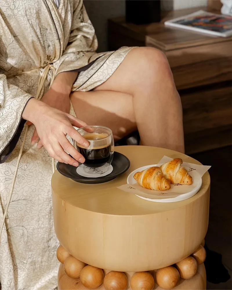 A relaxing morning experience at KHAI Hotel featuring a woman in a kimono enjoying coffee with branded coaster and croissants